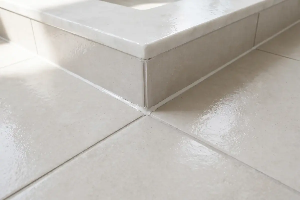 Porcelain floor tile meeting a shower curb with even grout lines and a caulked corner