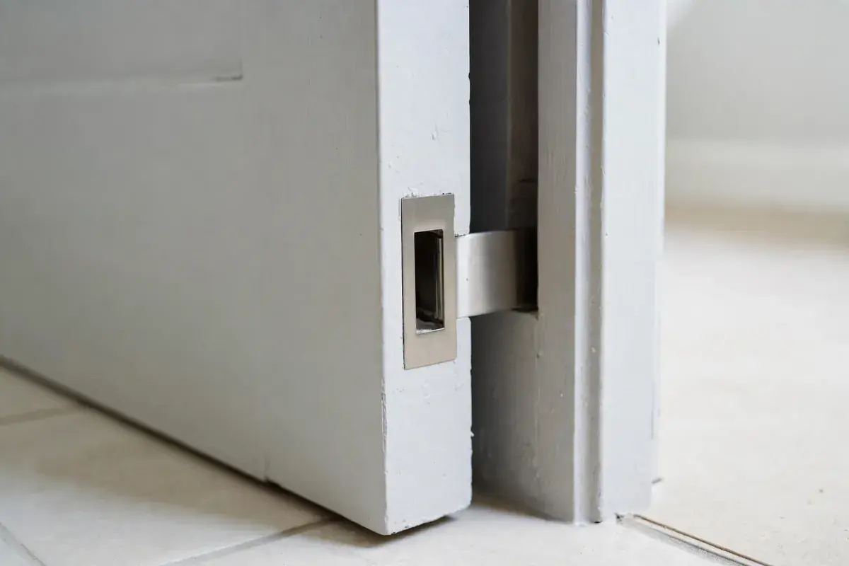 Flush pocket door pull in a narrow bathroom doorway beside a light tile floor